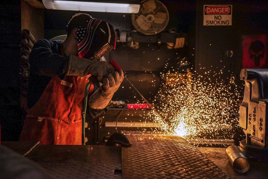 A sailor uses a flame cutting machine to shape pipes.