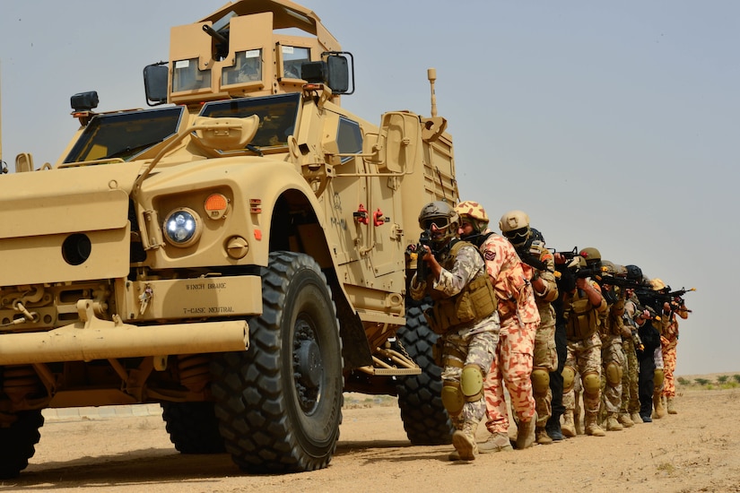 Troops with guns move forward next to truck