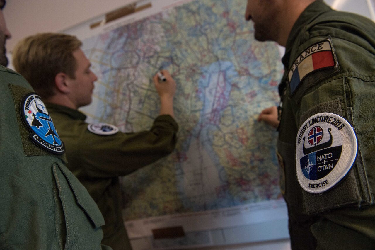 Three men in flight suits plan a flight on a wall map.