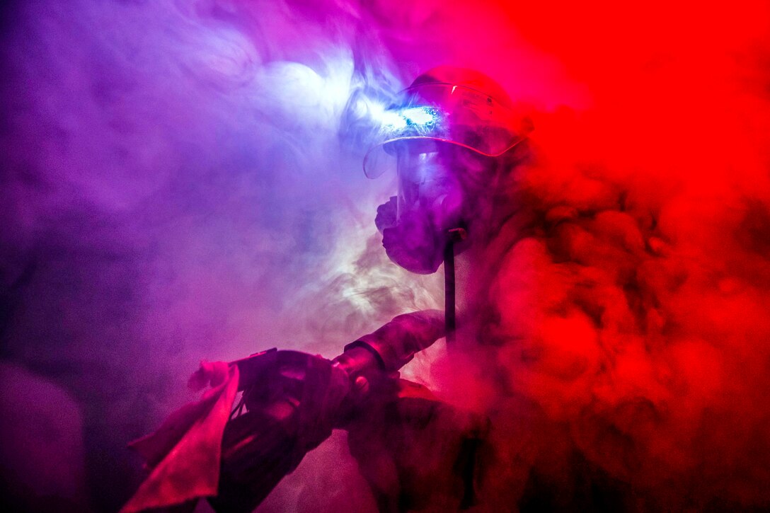 A sailor walks through thick smoke in close quarters.