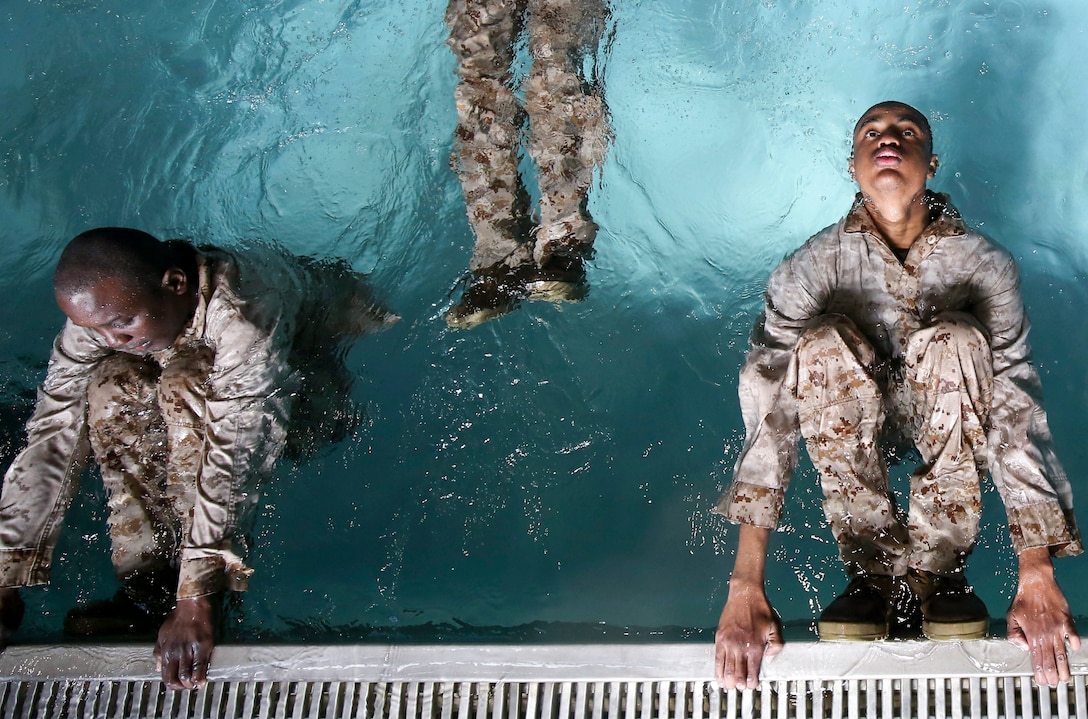 Two Marine recruits hold onto the edge of a pool.