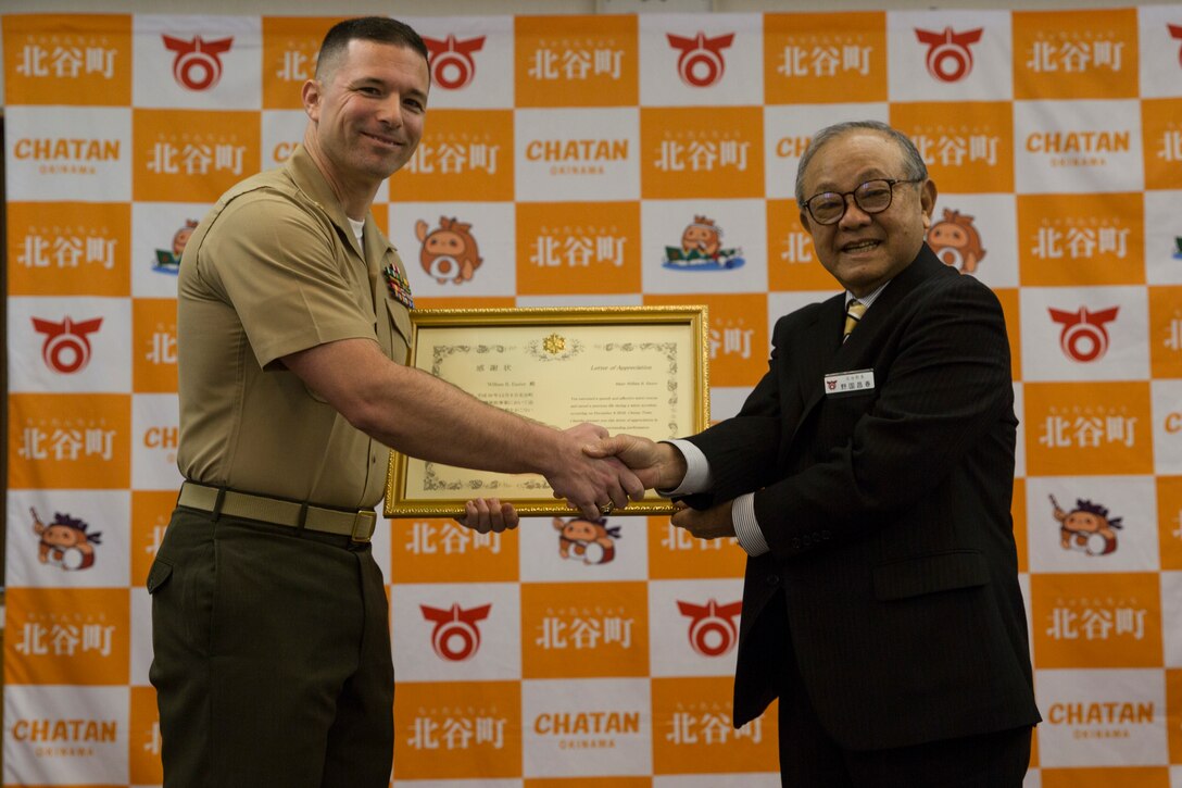 Maj. William Easter, left, a theatre security cooperation officer with III Marine Expeditionary Force, receives a letter of appreciation from Masaharu Noguni, the Mayor of Chatan, right, at the Chatan Town Office, Okinawa, Japan, Jan. 22, 2019. Mayor Noguni presented Easter with the award for aiding in the rescue of a pregnant woman who was a quarter of a mile away from the shoreline struggling to swim ashore. (U.S. Marine Corps photo by Lance Cpl. Hannah Hall)
