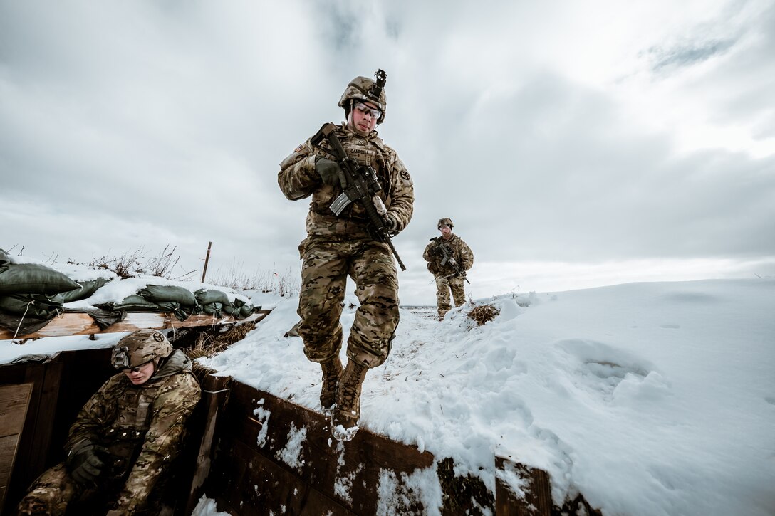 A soldier jumps into a trench with two soldiers behind.