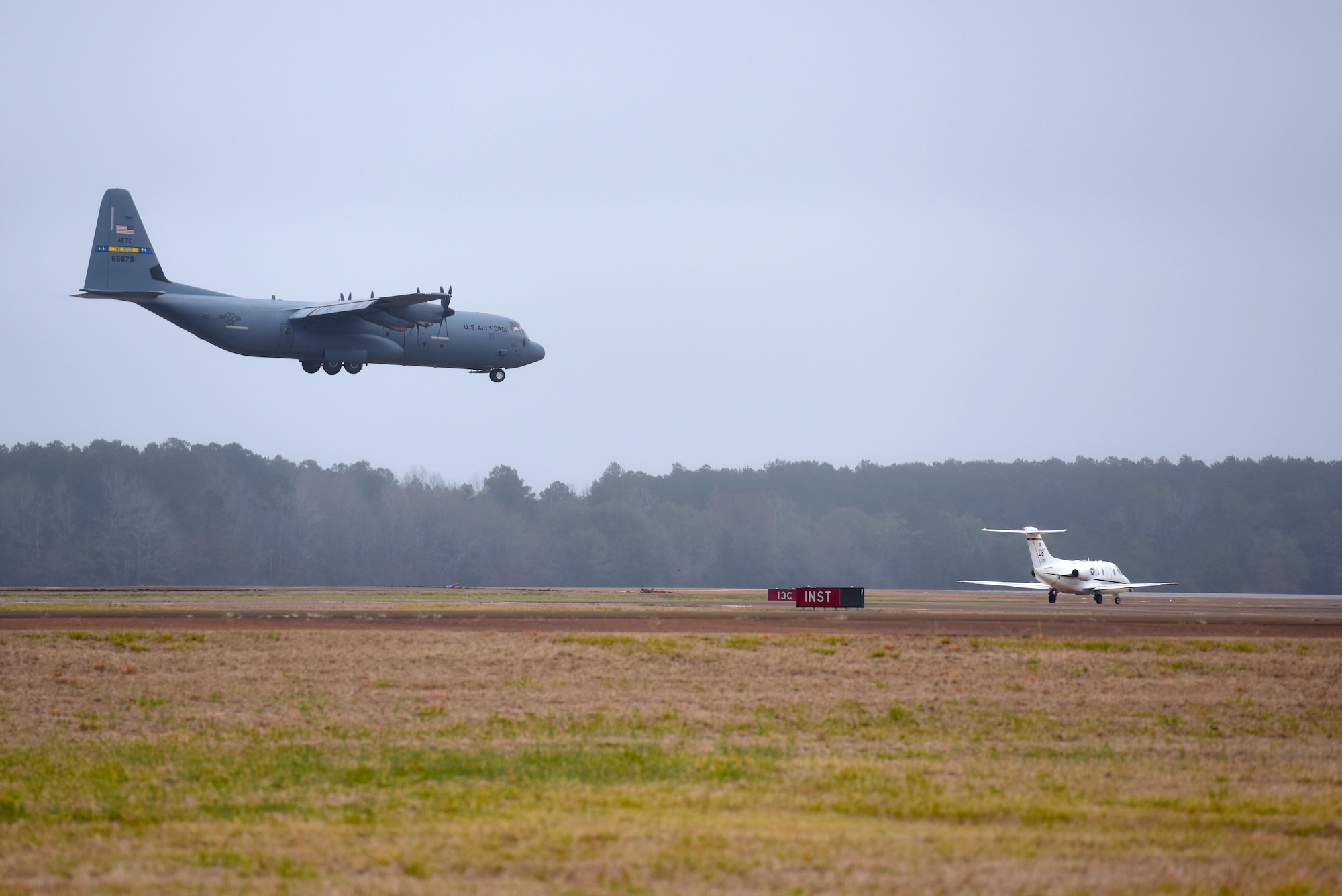 A C-130J Hercules, assigned to Little Rock Air Force Base, Arkansas, lands while a T-1A Jayhawk, assigned to the 48th Flying Training Squadron, waits for takeoff Feb. 5, 2019, on Columbus Air Force Base, Mississippi. Pilots who are selected to fly airlift or tanker aircraft must first fly the T-1 in Specialized Undergraduate Pilot Training. (U.S. Air Force photo by Senior Airman Beaux Hebert)