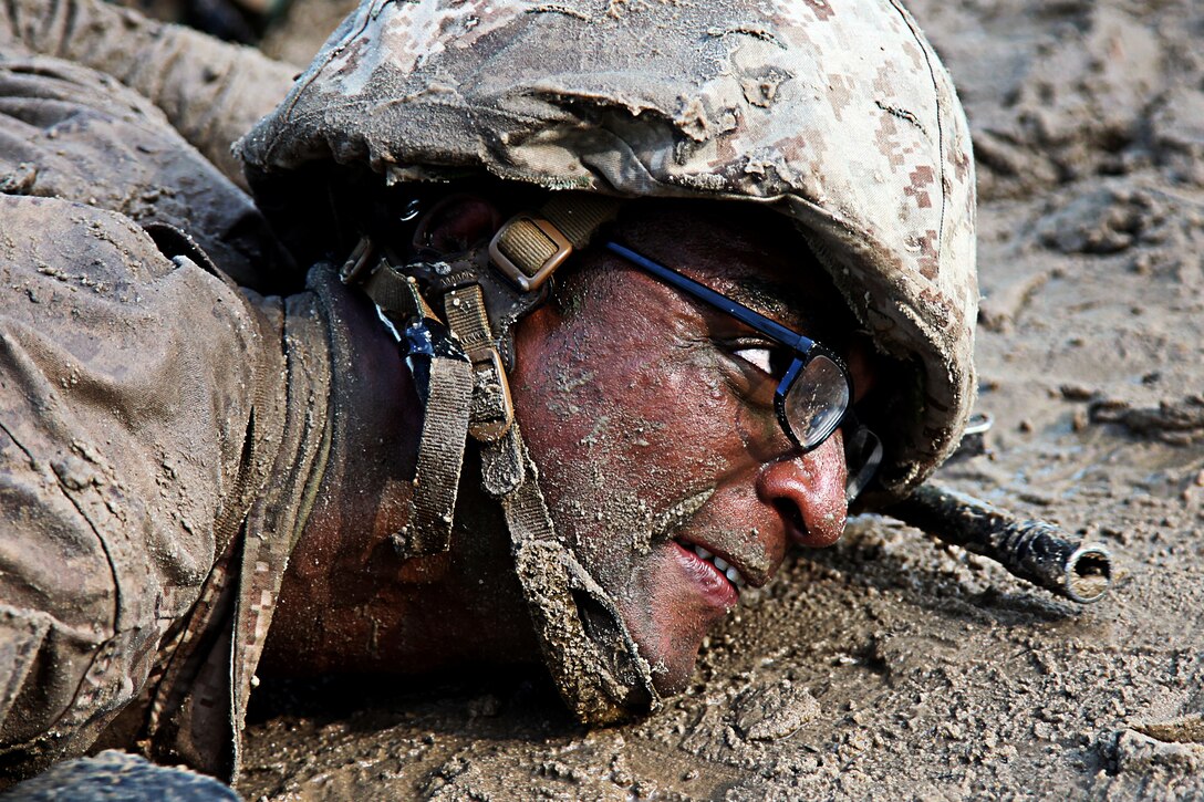 A Marine recruit crawls through some mud.