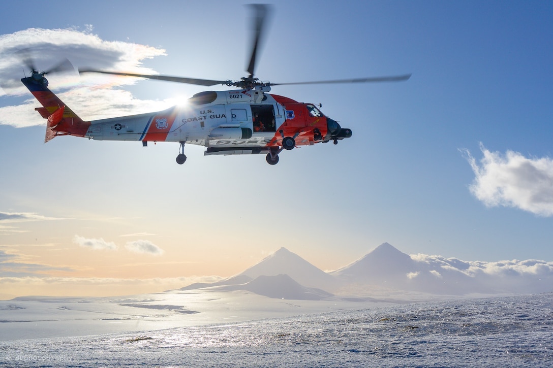 A helicopter flying over water with a volcano in the background