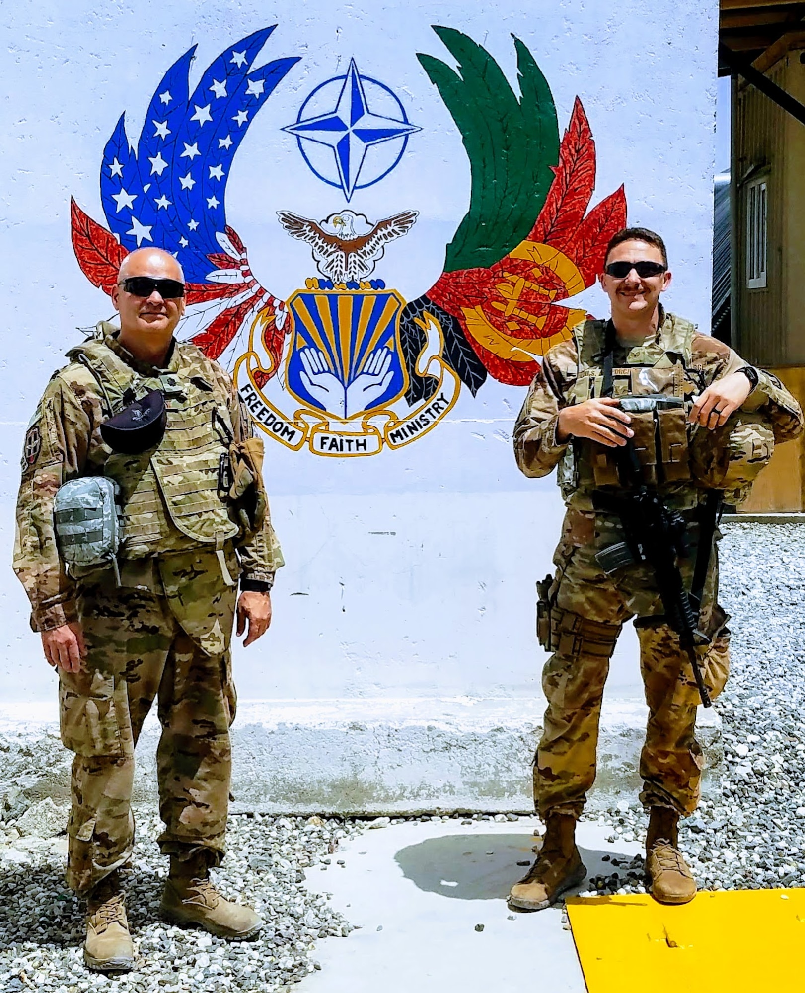 U.S. Air Force Lt. Col. John Shipman, Train, Advise, Assist Command-Air chaplain and Staff Sgt. Tony Hanks, 307th Bomb Wing religious affairs specialist stand by a mural at Hamid Karzai International Airport in Kabul, Afghanistan, July 12, 2018. Hanks was responsible for the safety of Shipman during their deployment. Chaplains are non-combatants and do not carry weapons.  (Courtesy photo)