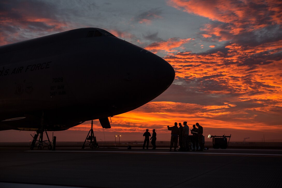 The nose of a military jet is silhouetted  against an orange sky.