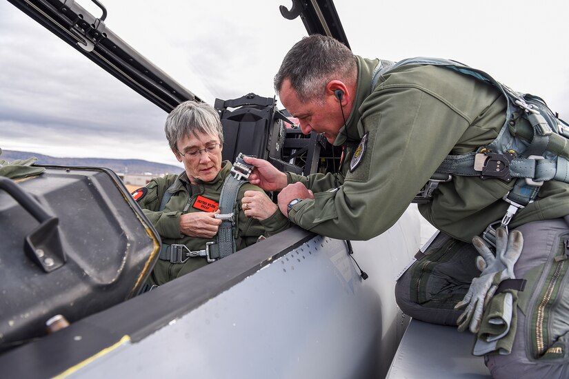 A man straps a lady into airplane cockpit.