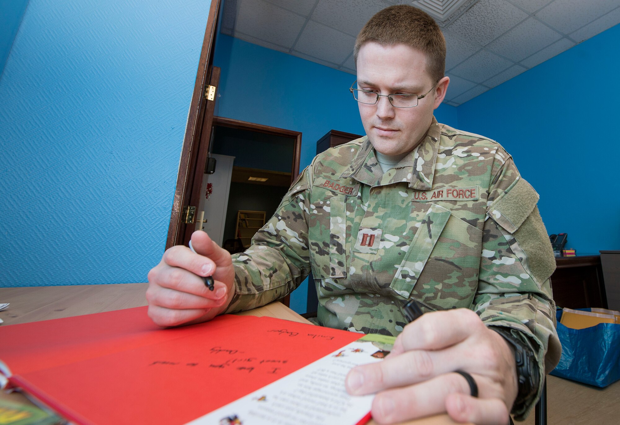 U.S. Air Force Capt. Nathan Badger, 34th Intelligence Squadron flight commander, writes messages to his children in a book as part of United Service Organizations (USO) Qatar’s Reading Program Feb. 8, 2019, at Al Udeid Air Base, Qatar. The USO reading program allows service members to record themselves reading books to send back to their children. Program participants can write messages in the books and send them to their children along with the video recording. (U.S. Air Force photo by Tech. Sgt. Christopher Hubenthal)
