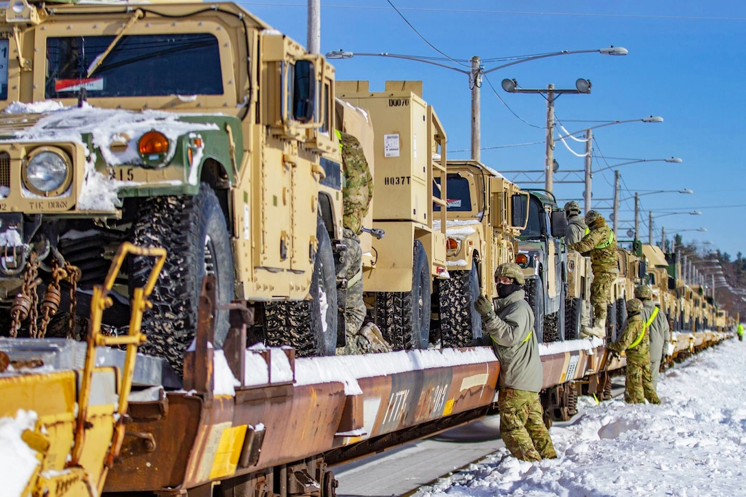 Soldiers standing in snow secure military vehicles on a railway.