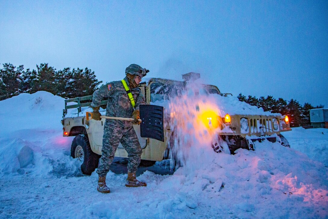 A soldier shovels  snow around a Humvee.