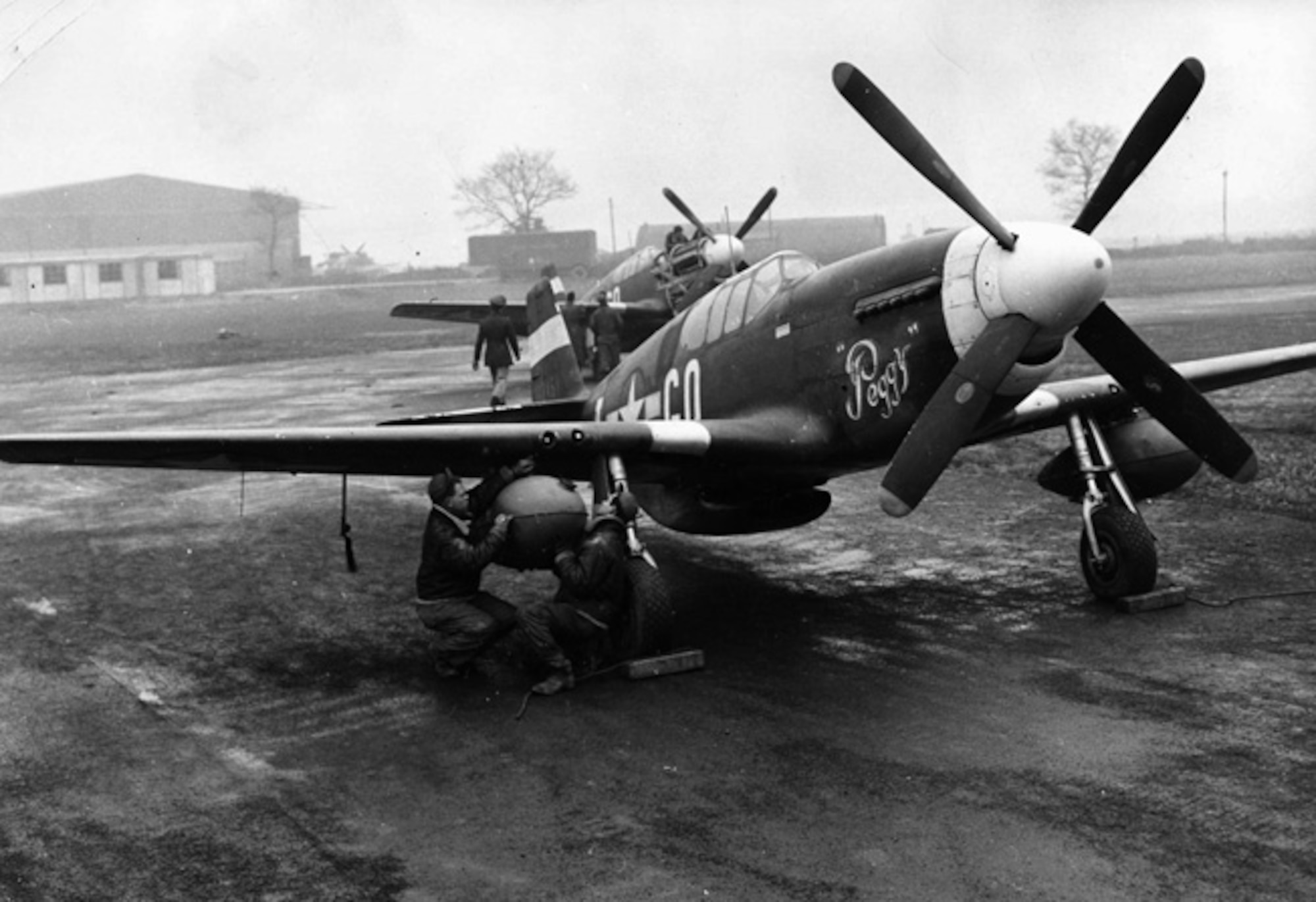 Two P-51D Mustangs at an English airfield in early 1944. The ground crew is fitting the second of two underwing fuel tanks, which allowed the Mustangs to escort American strategic bombers to their targets inside Germany, engage German fighters and return to their bases in England. (U.S. Air Force photo)