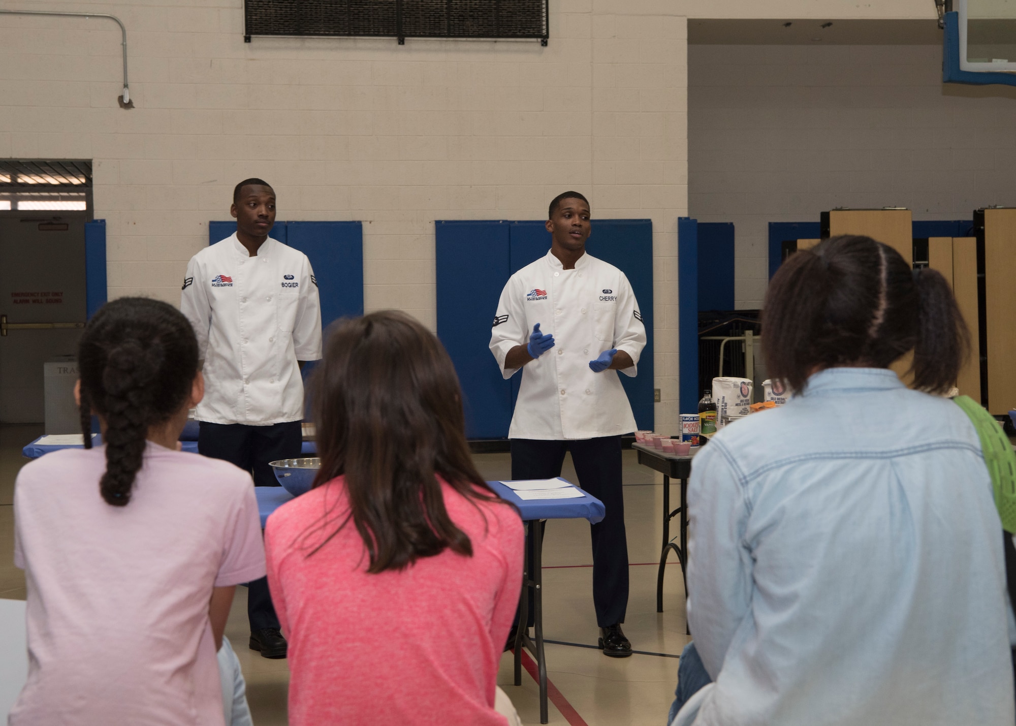 (From left to right) Airman 1st Class Dominick Bogier, 49th Force Support Squadron food service apprentice and Airman 1st Class Malik Cherry, 49th FSS food service specialist, brief youth baking competition teams on the challenge, Jan. 30, 2019, on Holloman Air Force Base, N.M. Five teams from the Youth and Teen Center participated in a cookie baking challenge to win golden spatulas. (U.S. Air Force photo by Airman Autumn Vogt)
