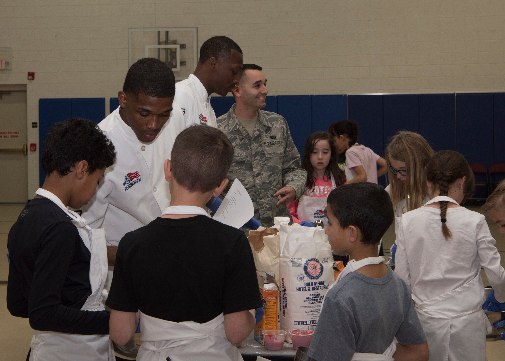 (From left to right) Airman 1st Class Malik Cherry, 49th Force Support Squadron food service specialist, and Airman 1st Class Dominick Bogier, 49th FSS food service apprentice, assist youth baking competition teams with gathering cookie ingredients, Jan. 30, 2019, on Holloman Air Force Base, N.M. Seventeen members of the Youth and Teen Center signed up for a cookie baking competition and the competition lasted two and a half hours. (U.S. Air Force photo by Airman Autumn Vogt)