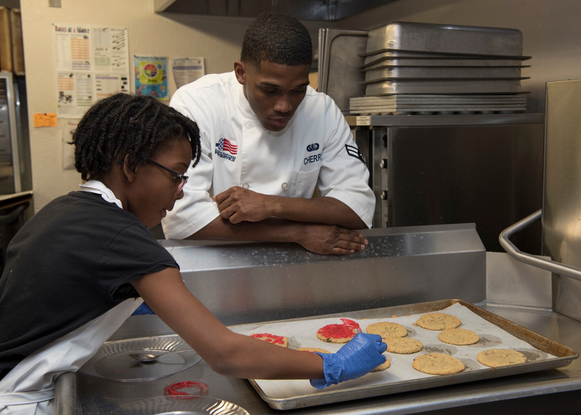 (From left to right) Ysabelle Smith, This is Sparta team leader (left), receives advice on making frosting hearts for cookies from Airman 1st Class Malik Cherry, 49th FSS food service specialist (right), Jan. 30, 2019, on Holloman Air Force Base, N.M. Seventeen members of the Youth and Teen Center signed up for a cookie baking competition and the competition lasted two and a half hours. (U.S. Air Force photo by Airman Autumn Vogt)