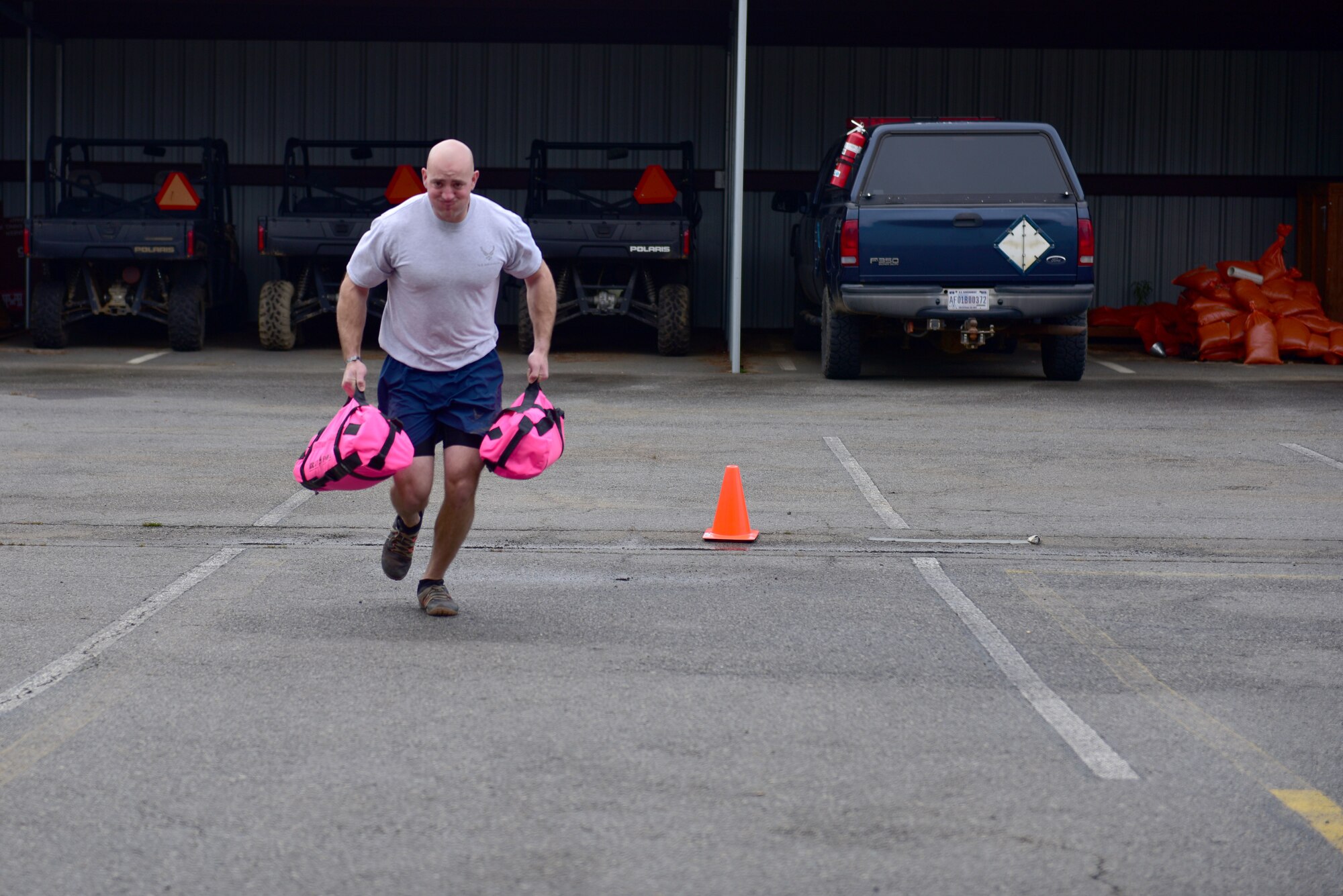 A man wearing the Air Force physical training uniform runs with 2 pink sandbags.