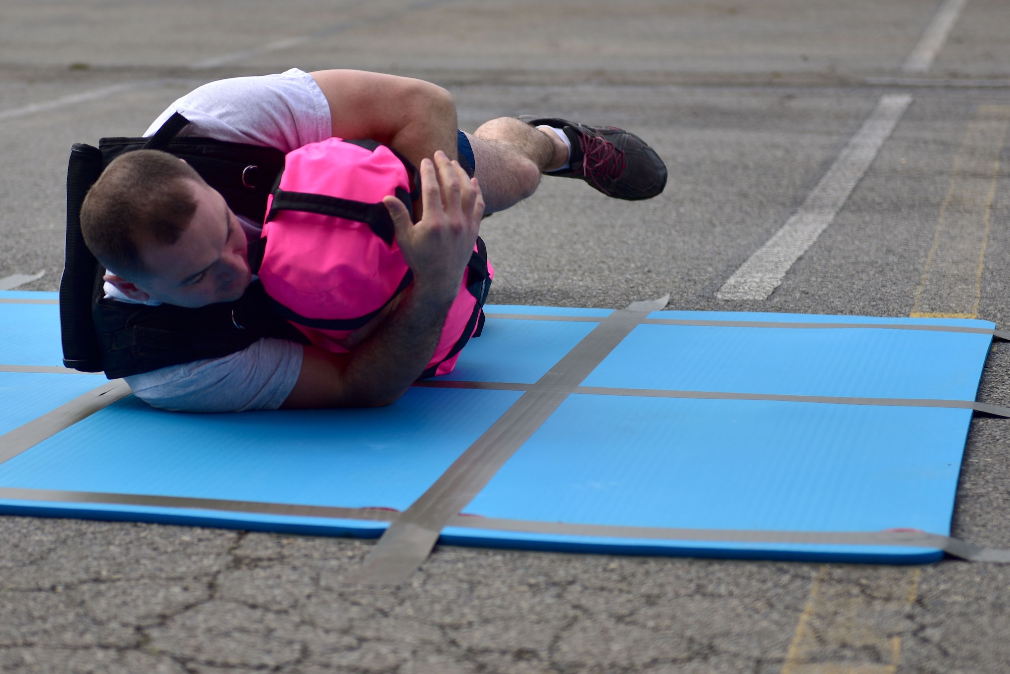 A man rolls with a pink sandbag and a weighted vest.
