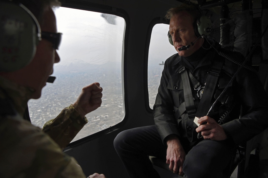 Two men talk on board a helicopter.