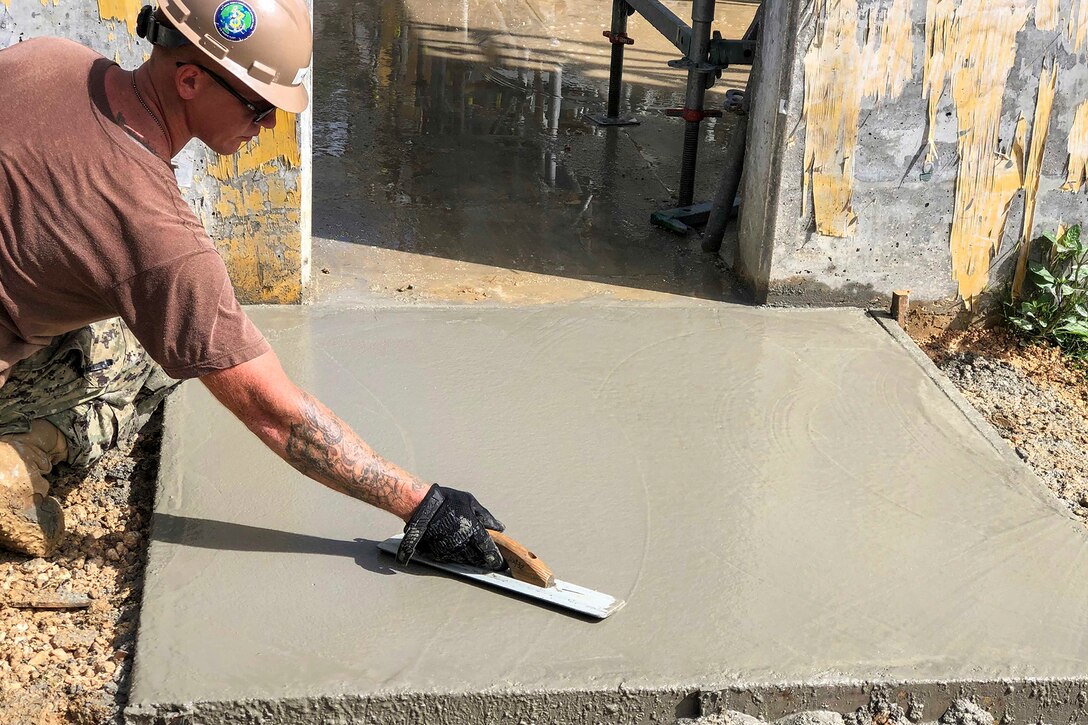 A service member smooths a concrete pad.