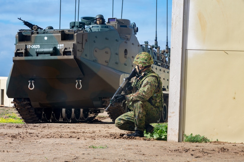 A Japan Ground Self-Defense Force soldier patrols alongside an assault amphibious vehicle.