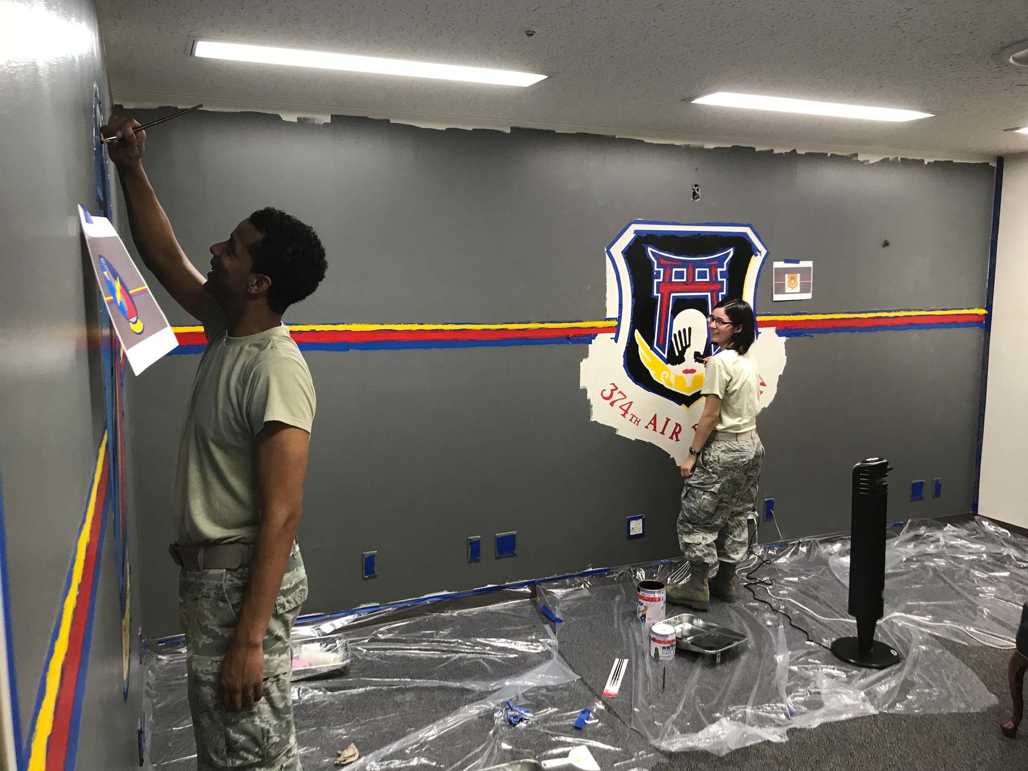 Tech Sgt. Adam Bethea, 374th Operations Support Squadron aircrew flight equipment craftsman, and then Senior Airman Darion Duverney, 374 OSS weather journeyman, paint a mural in the conference room at Yokota Air Base, Japan, Jul. 20, 2018.