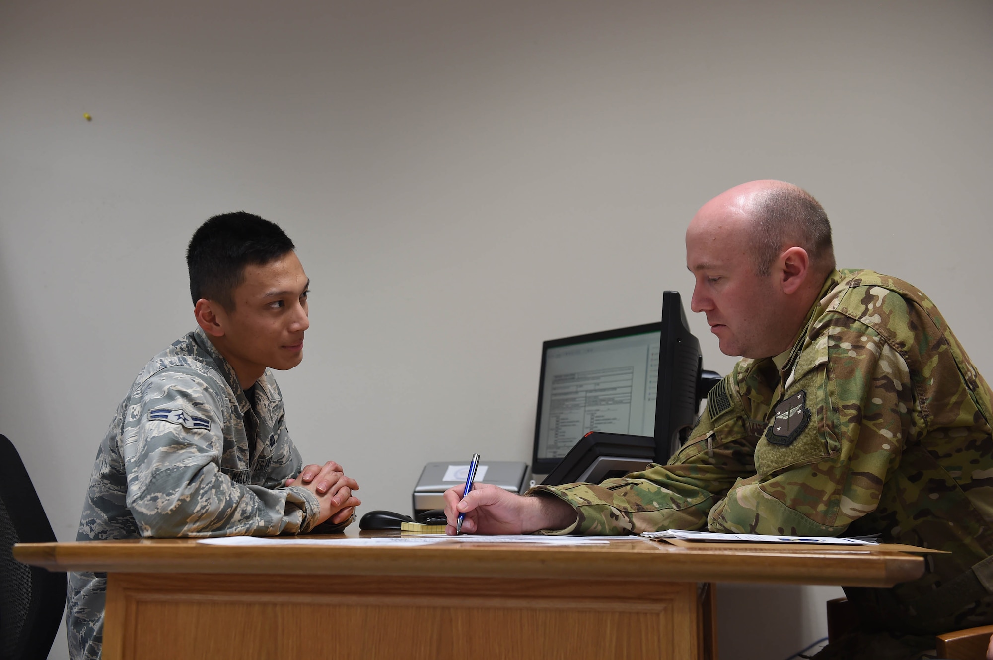 Two Airmen sit a desk with a computer