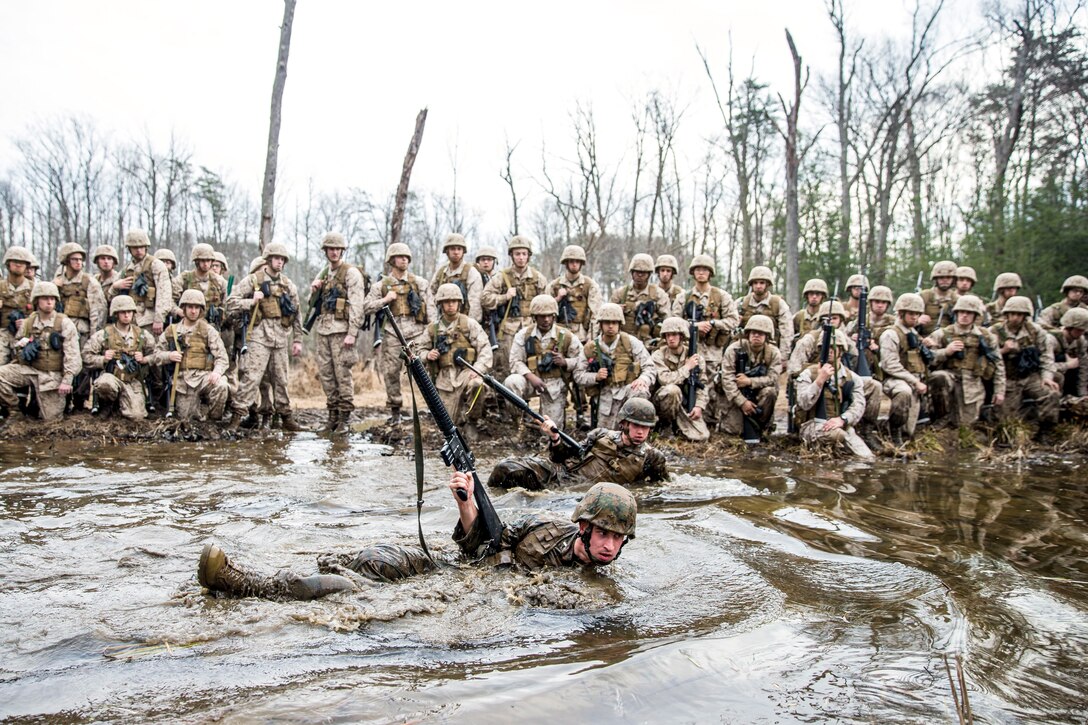 Two Marines move through a muddy puddle as others watch.