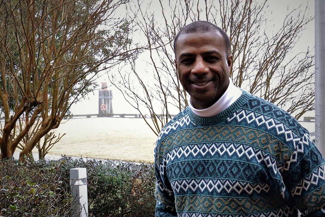 Man poses for photo by standing outside. Pier is in the background.