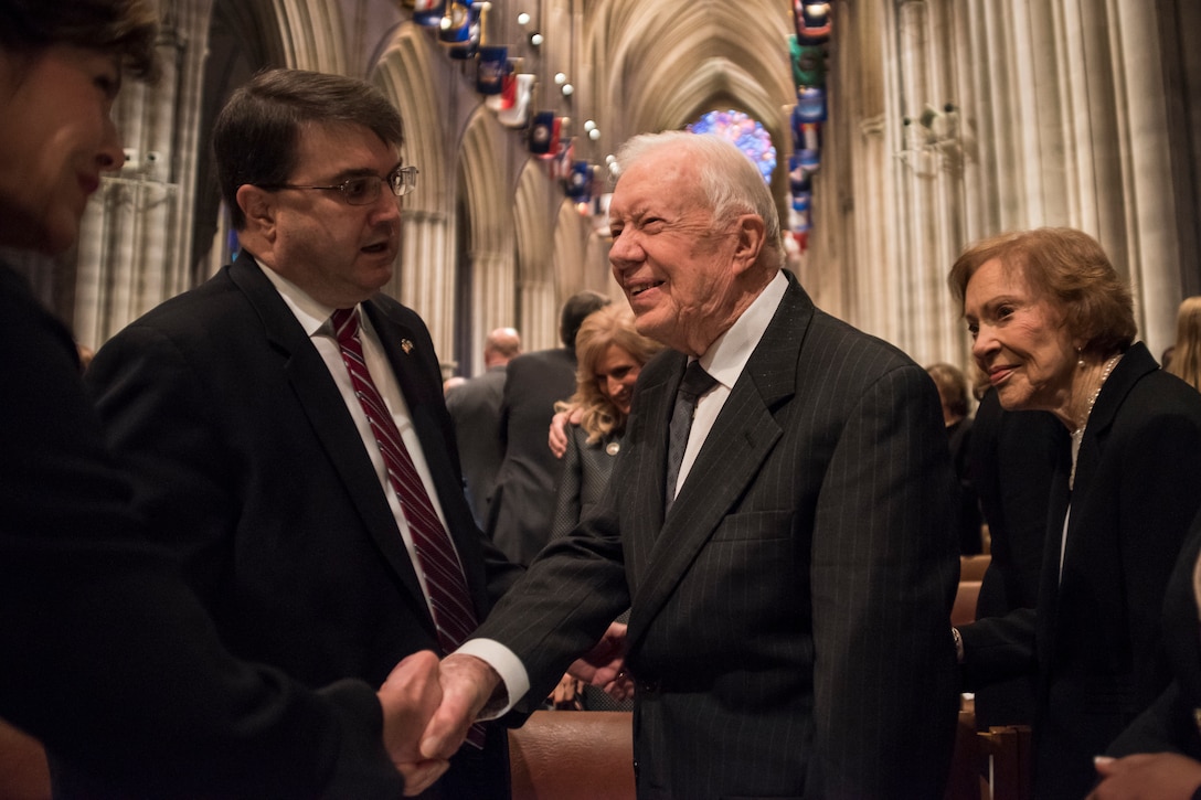 An older man shakes hands with someone else in a cathedral.