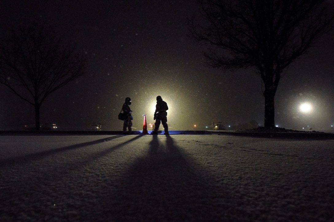 Airmen, shown in silhouette, stand in a snowy field at night.