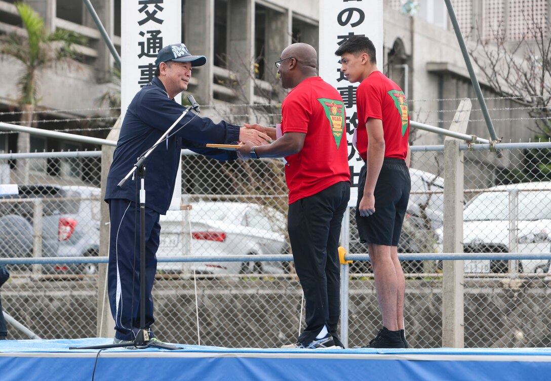 Masanori Matsugawa, Mayor of Ginowan City, presents a plaque to the team at representing Futenma Air Station at Marine Corps Air Station Futenma, Okinawa, Japan, Jan. 19, 2019. The Futenma team placed second in the 42nd Ginowan Traffic Safety Relay Race. (U.S. Marine Corps photo by Lance Cpl. Savannah Mesimer)