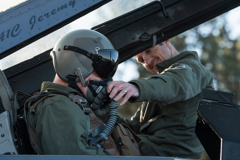 A pilot helps another pilot with his oxygen mask
