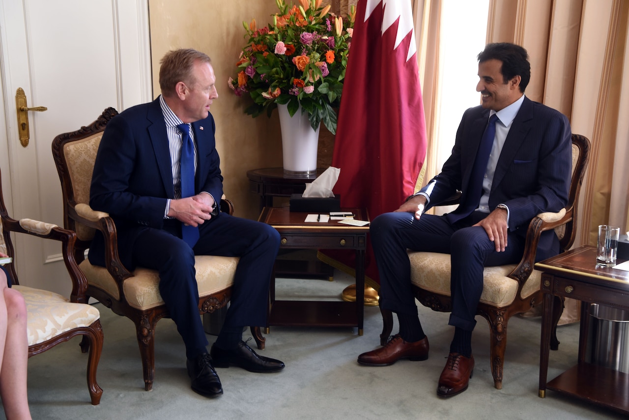 Two men sit in chairs and talk.