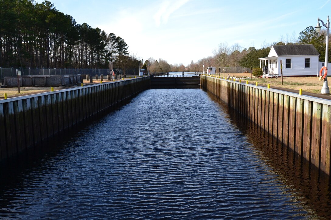 A view of the Deep Creek Lock, a waterway with wooden planks on the sides and a small house on the right side. the left side has trees