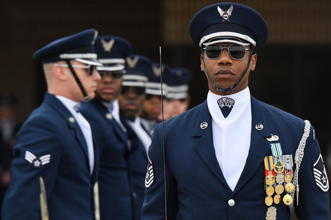 An airman stands in front of line of airmen during a performance.