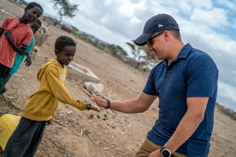 A soldier in civilian clothing slaps palms with a child while two others look on.