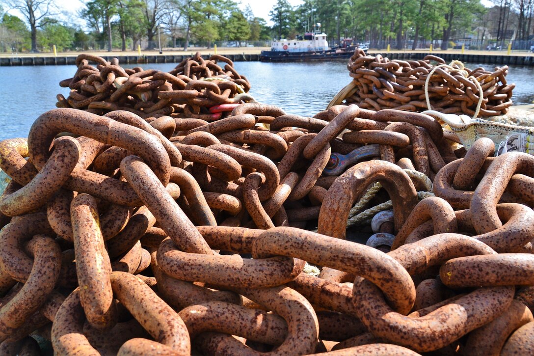 A pile of rusted chain is in the foreground and in the background is a moored boat.