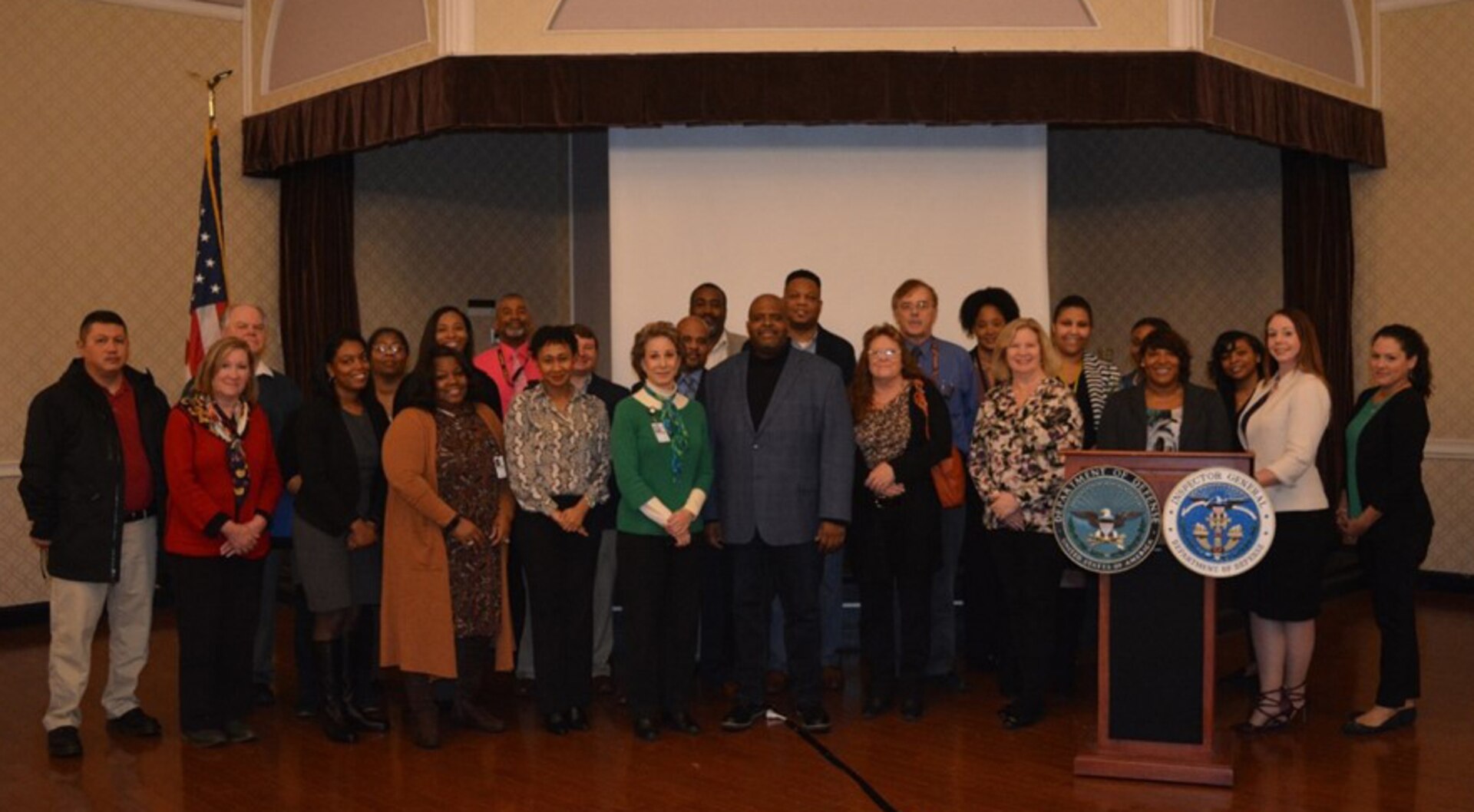 Group shot of males and females standing near a podium and an American flag