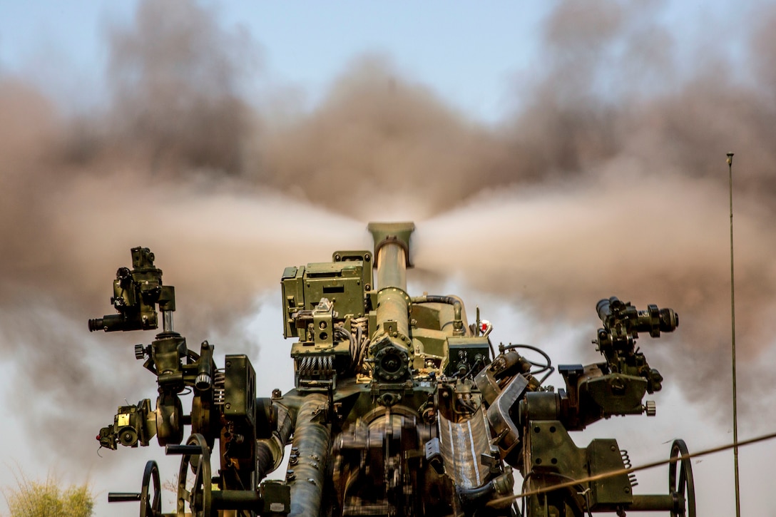 Smoke blasts out symmetrically from a howitzer, shown from behind.