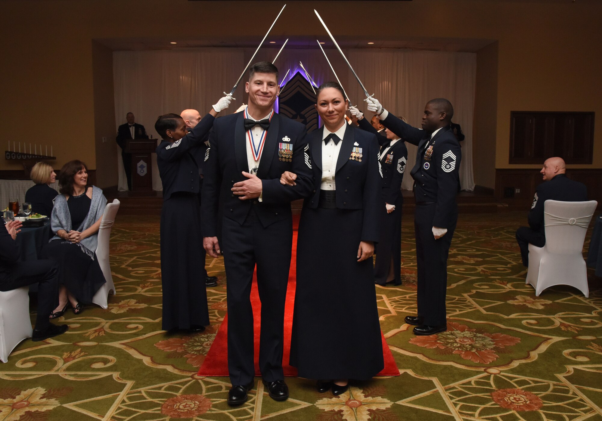 U.S. Air Force Senior Master Sgt. Kevin Lambert, 81st Security Forces Squadron operations superintendent, and his wife, Chief Master Sgt. Sevin Balkuvvar, 96th Logistics Readiness Squadron materiel management flight superintendent, Eglin Air Force Base, Florida, pose for a photo after walking under an archway of sabers held by Keesler's Chief Master Sgts. during the Chief Induction Ceremony inside the Bay Breeze Event Center at Keesler Air Force Base, Mississippi, Feb. 15, 2019. Five Keesler Airmen earned their chief master sergeant stripe during the 2019 promotion release. Air Force officials selected 479 senior master sergeants for promotion to chief master sergeant out of 2,241 eligible for a selection rate of 21.37 percent. Chief master sergeants make up one percent of the Air Force enlisted force. (U.S. Air Force photo by Kemberly Groue)