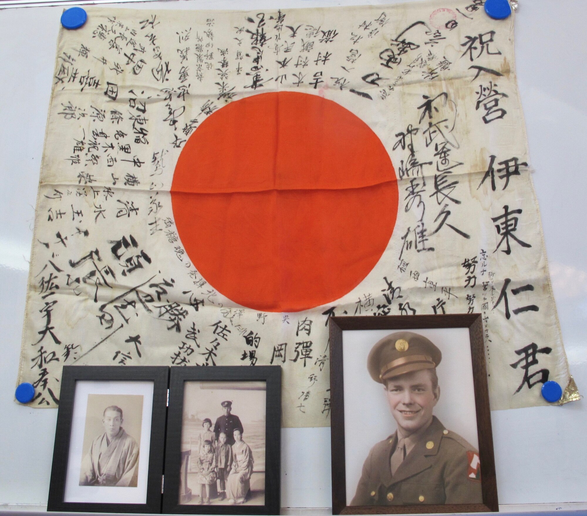 Photos of Masashi Ito (left) and Cpl. Lowell Armstrong (right) sit on display with a Japanese war flag during a flag return ceremony in Takasaki, Japan, Feb. 14, 2019. Armstrong acquired the flag during World War II. U.S. Air Force Senior Master Sgt. William Armstrong, 8th Logistics Readiness Squadron deployment and distribution flight superintendent and Cpl. Armstrong’s grandson, traveled to Japan and returned the flag to Ito’s nephews, Michio Miki and Hideo Ito. (Courtesy photo, Obon Society)