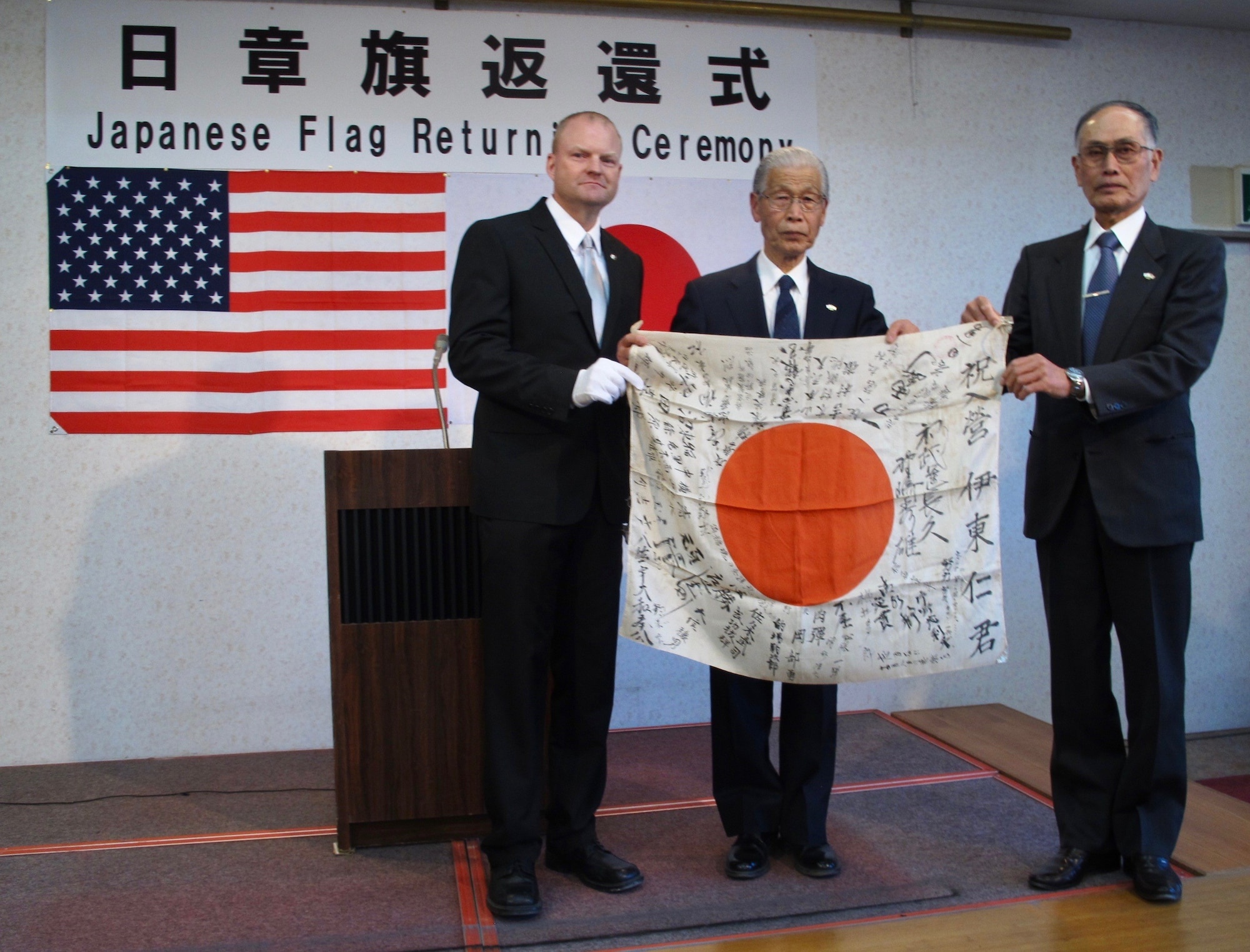 U.S. Air Force Senior Master Sgt. William Armstrong, 8th Logistics Readiness Squadron deployment and distribution flight superintendent, (left), hands a Japanese flag to Michio Miki (middle) and Hideo Ito, Masashi Ito’s nephews, during a flag return ceremony in Takasaki, Japan, Feb. 14, 2019. Armstrong’s grandfather acquired Miki and Ito’s uncle’s flag during World War II. (Courtesy photo, Obon Society)