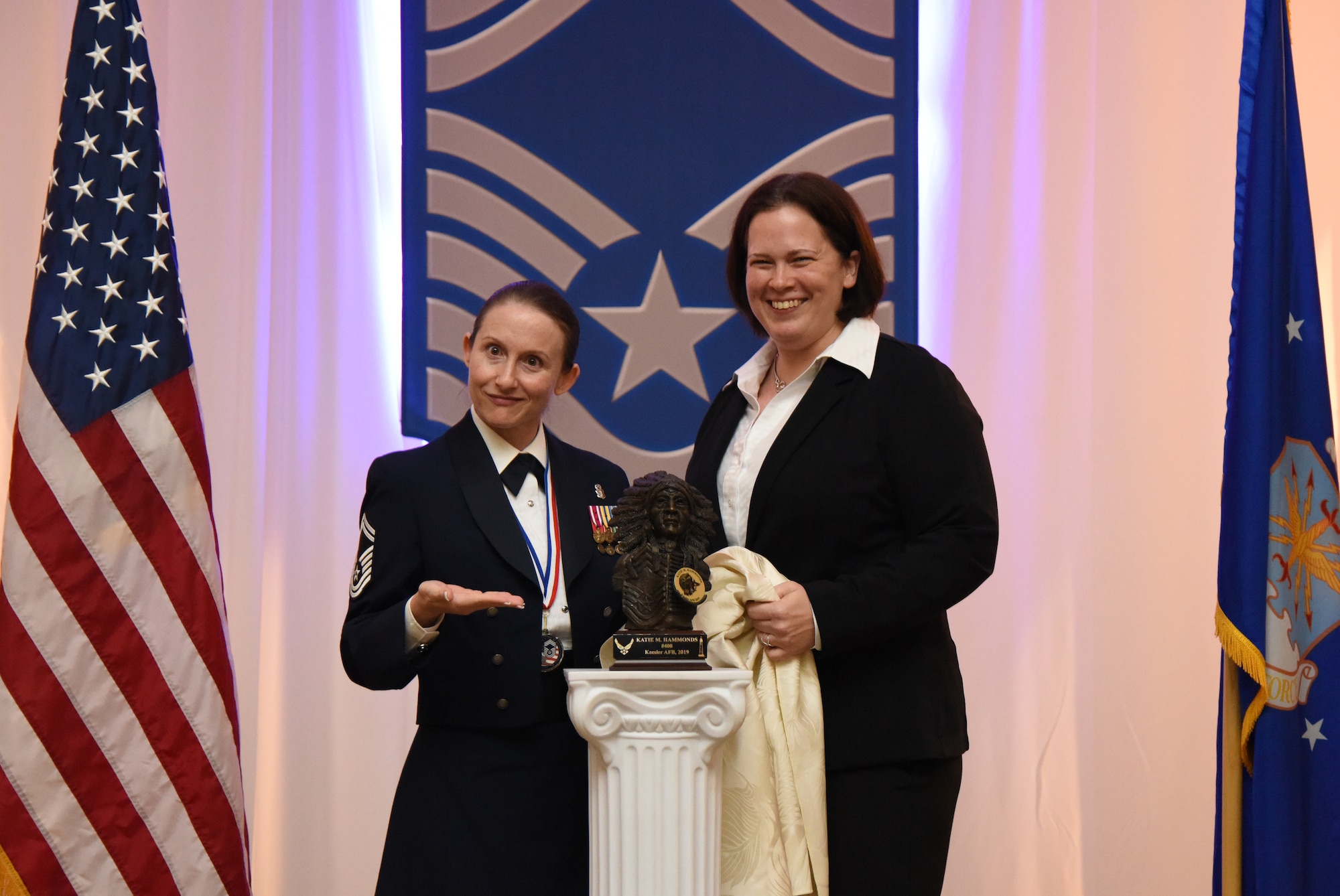 U.S. Air Force Senior Master Sgt. Katie Hammonds, 81st Medical Support Squadron medical logistics flight chief, is joined by her friend, Erin Marchand, as they unveil a statue presented to Hammonds during the Chief Induction Ceremony inside the Bay Breeze Event Center at Keesler Air Force Base, Mississippi, Feb. 15, 2019. Five Keesler Airmen earned their chief master sergeant stripe during the 2019 promotion release. Air Force officials selected 479 senior master sergeants for promotion to chief master sergeant out of 2,241 eligible for a selection rate of 21.37 percent. Chief master sergeants make up one percent of the Air Force enlisted force. (U.S. Air Force photo by Kemberly Groue)
