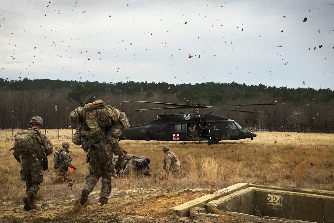 Army paratroopers run toward a helicopter.