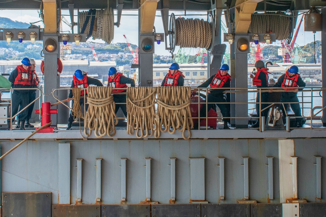 Several sailors on a ship pull ropes.