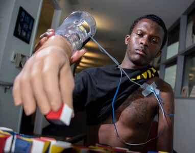 Army Staff Sgt. Kayshawn Porterfield practices picking up objects using a myoelectric prosthesis at Brooke Army Medical Center’s Center for the Intrepid at Joint Base San Antonio-Fort Sam Houston Feb. 21. A myoelectric-controlled prosthesis is an externally powered artificial limb that the user controls with electrical signals generated naturally with his own muscles.