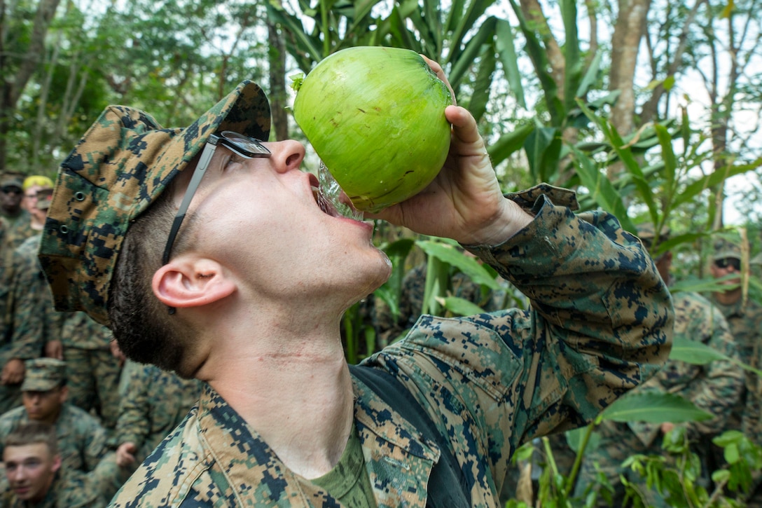 A Marine, shown in profile, drinks from a coconut he holds above his mouth.