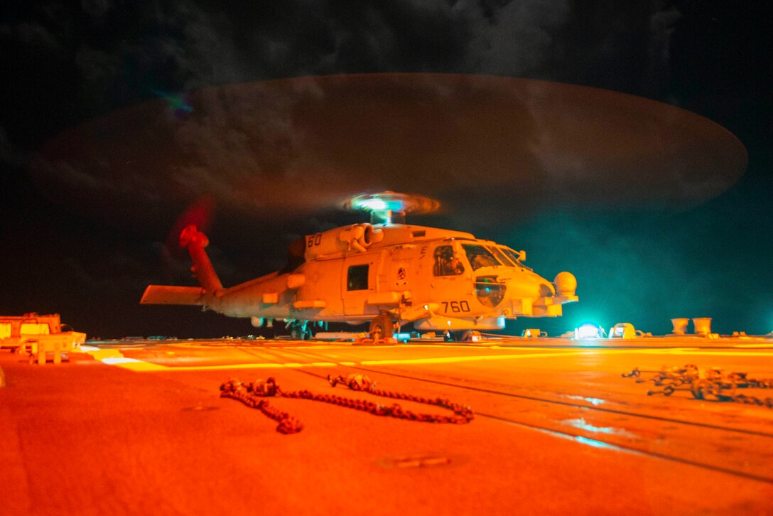 A helicopter sits on the deck of of a ship.