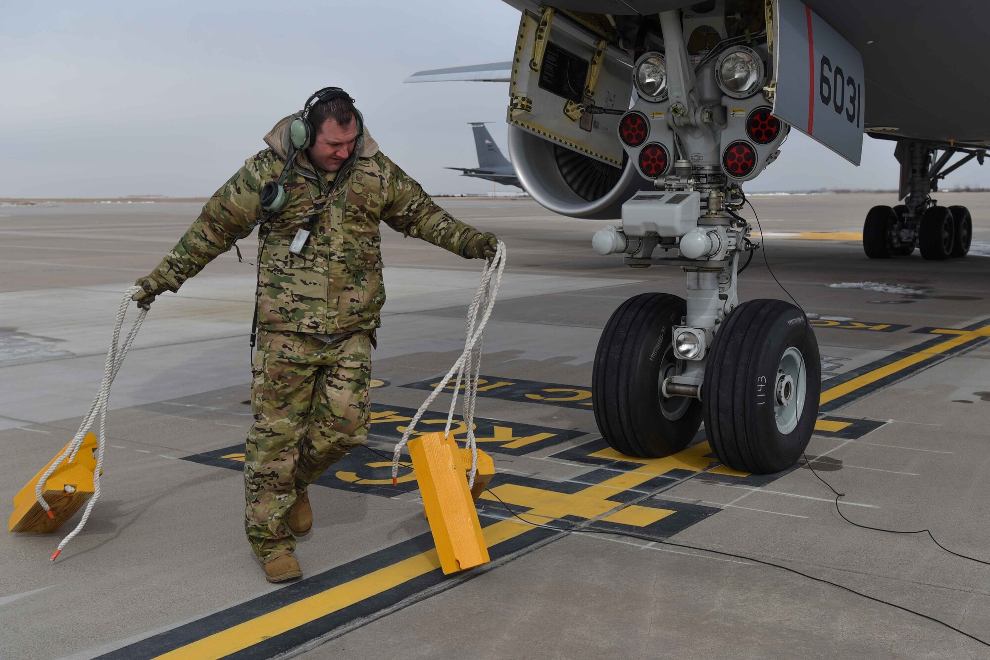 Master Sgt. Scott Perkins, 931st Aircraft Maintenance Squadron crew chief, pulls the chocks from underneath the KC-46A Pegasus before taxi Feb. 21, 2019, at McConnell Air Force Base, Kan. McConnell has taken various steps toward operationally flying the new aircraft, including facility improvements holding KC-46 simulators and a fuselage trainer. After all the procedures in the familiarization period are complete, McConnell will be able to operationally fly and refuel with the aircraft. (This photo has been altered for security purposes by blurring out identification badges) (U.S. Air Force photo by Airman 1st Class Alexi Myrick)